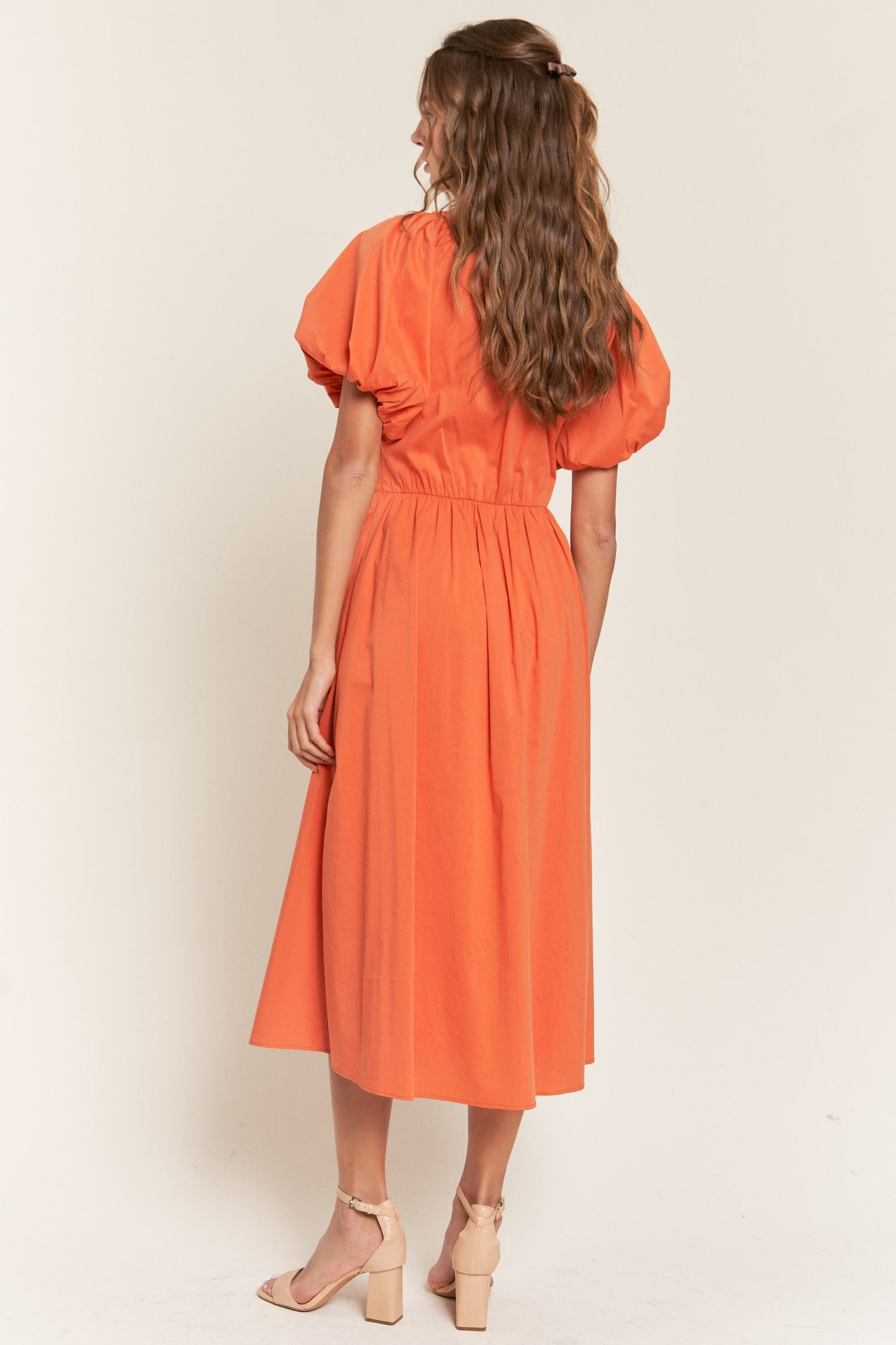 woman wearing an orange puff sleeve midi dress with a cinched waist and back pleats, shown from the back
