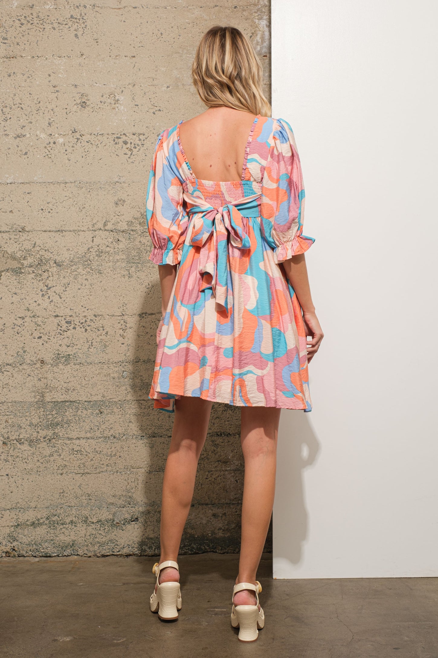 woman wearing a colorful short puff sleeve dress with a tie detail at the back