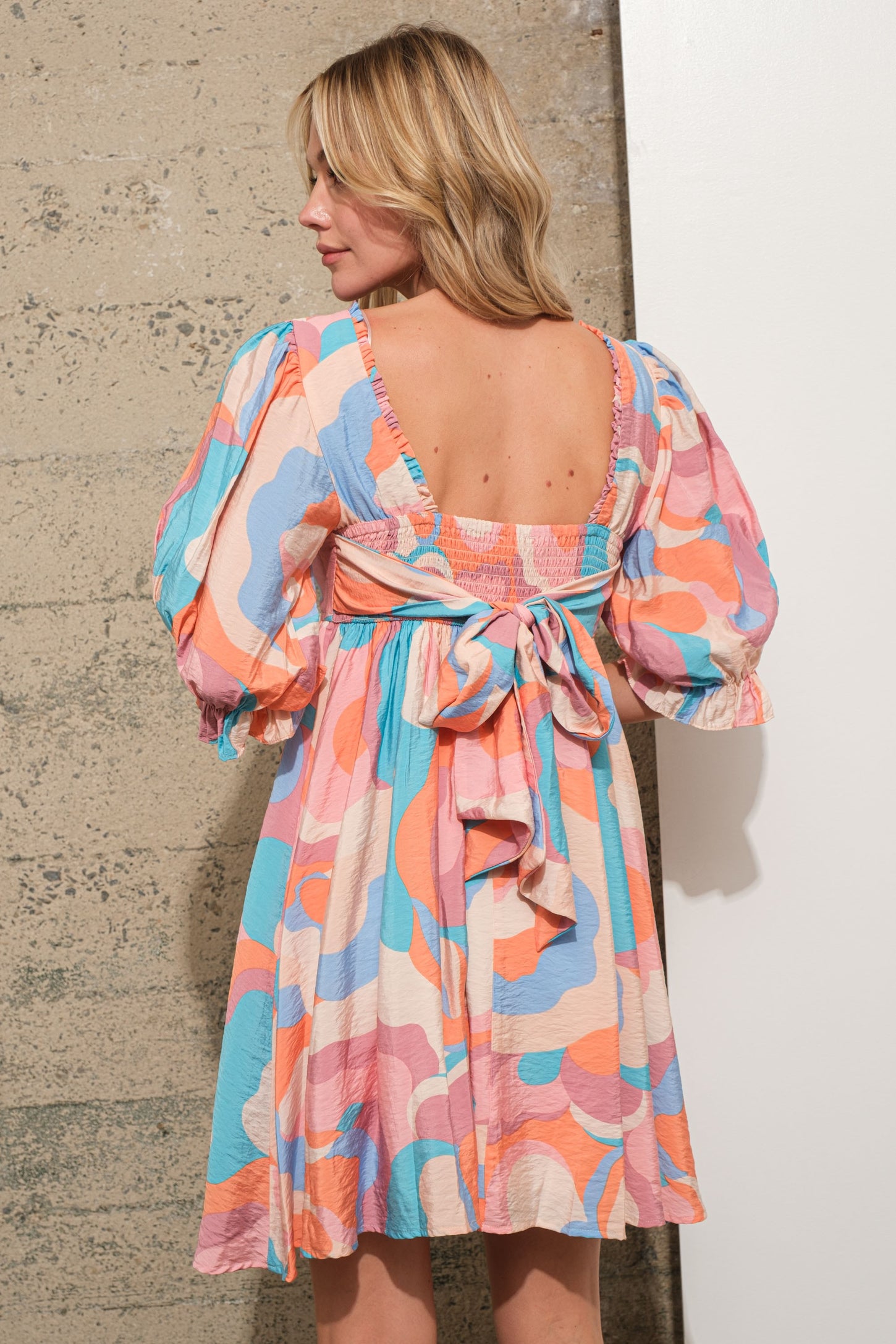 woman wearing a colorful abstract patterned short dress with puff sleeves and a bow detail at the back