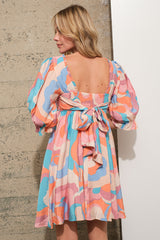 woman wearing a colorful abstract patterned short dress with puff sleeves and a bow detail at the back