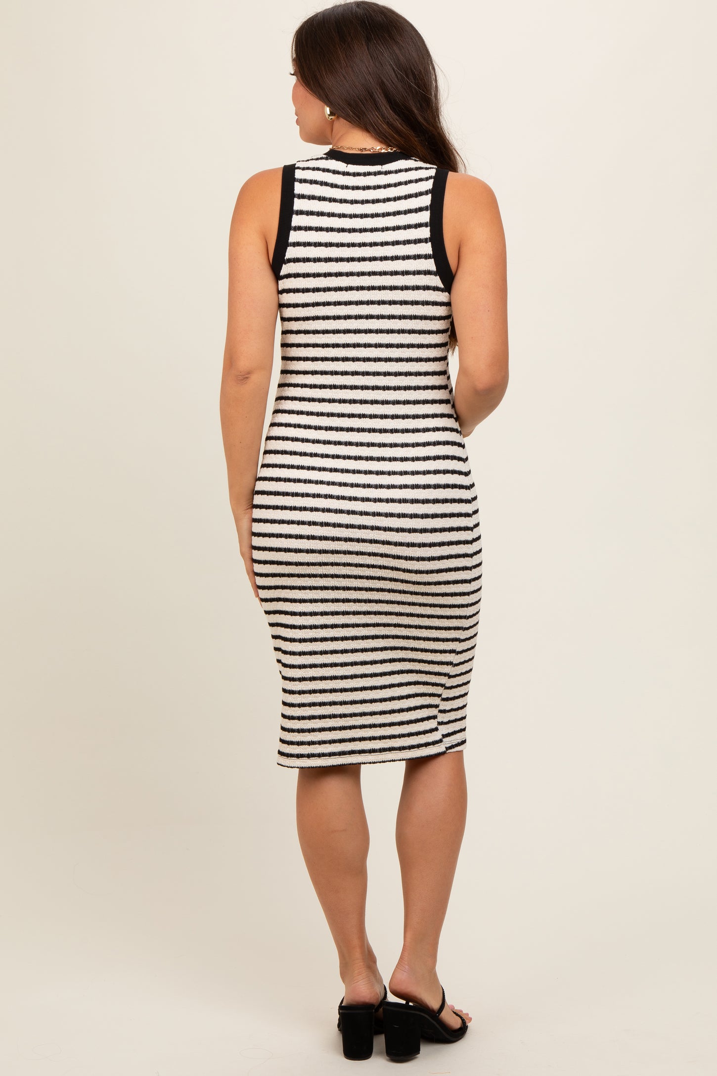 woman wearing a black and white striped maternity dress, showing a fitted style and knee-length cut from the back