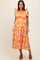woman wearing an orange floral maternity dress with tie straps and a smocked bodice, posing with a smile