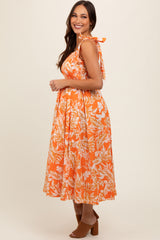 woman wearing an orange floral maternity dress with tie straps and a flowing skirt, revealing a baby bump