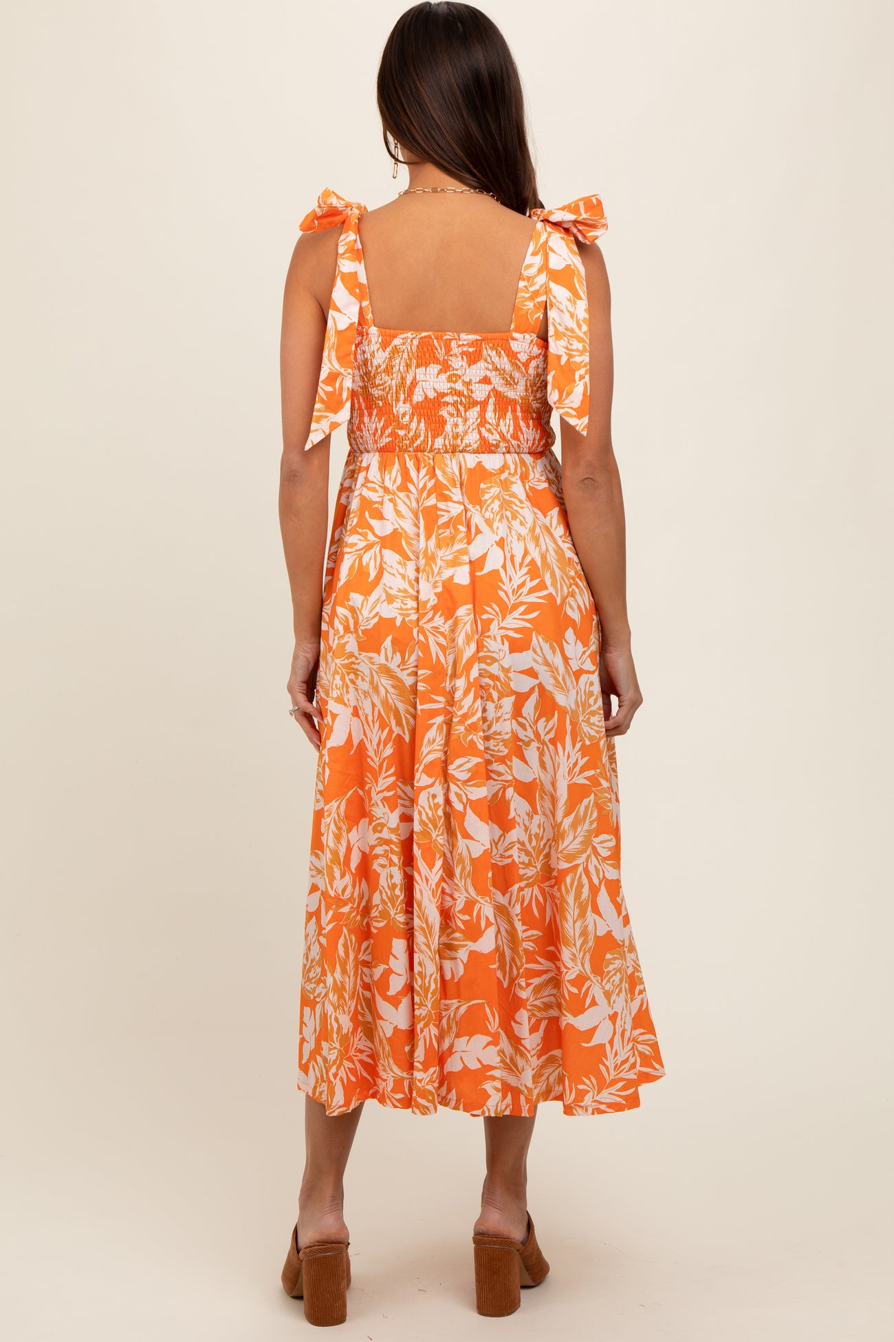 woman wearing an orange floral maternity dress with tie straps and a smocked bodice, showing her back