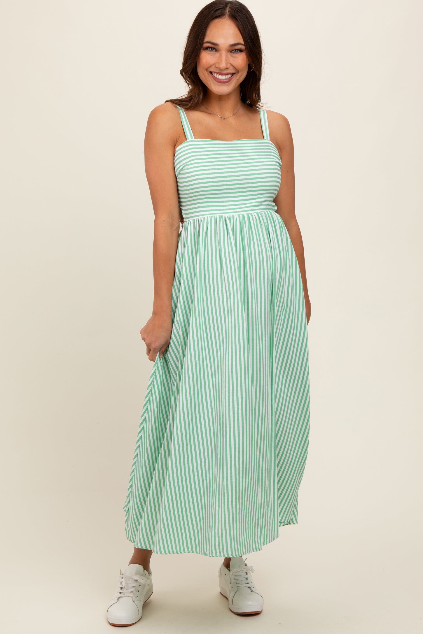 woman wearing a pastel green and white striped maternity dress with a square neckline and flowy skirt, standing and smiling