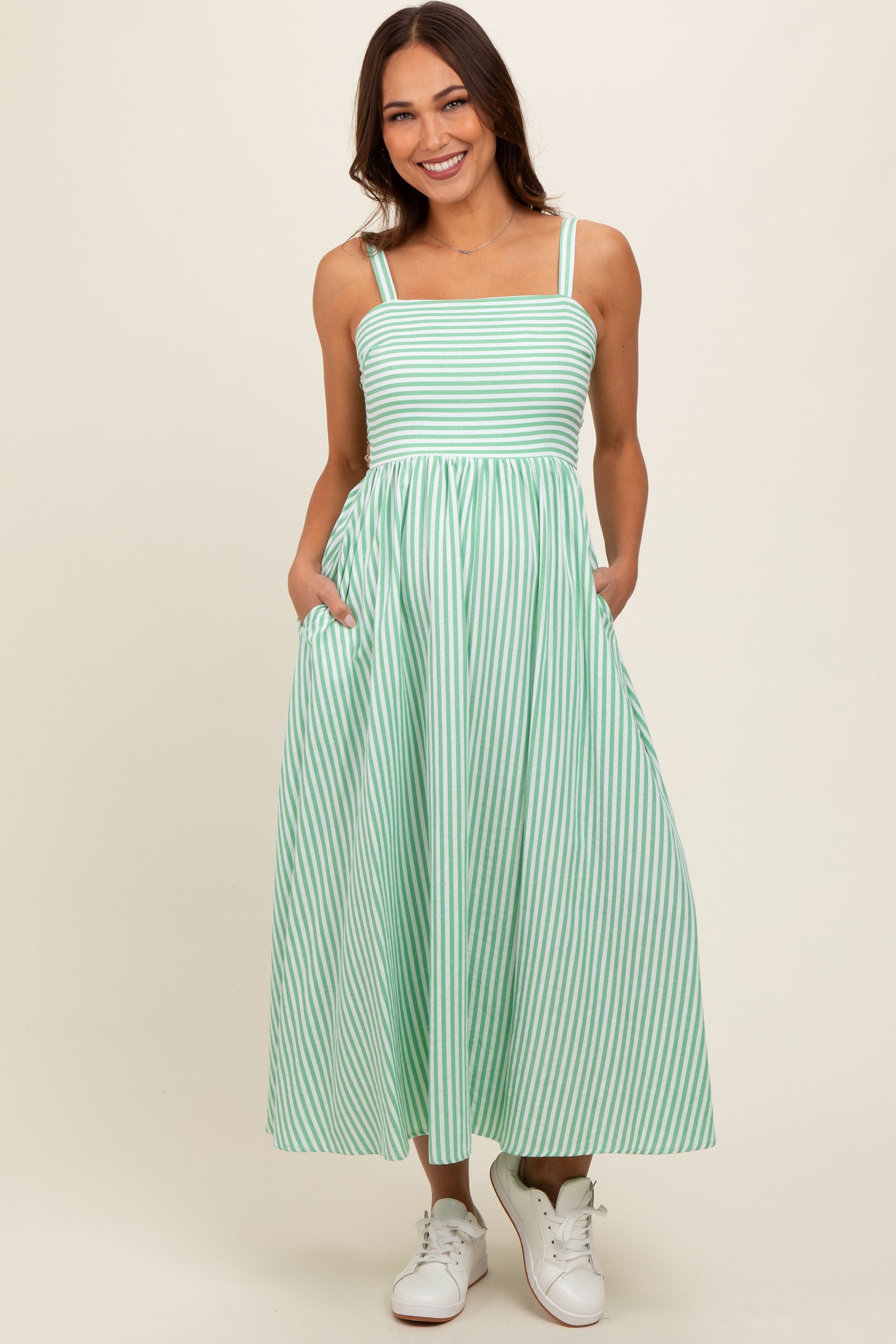 woman wearing a green and white striped maxi maternity dress with pockets and spaghetti straps