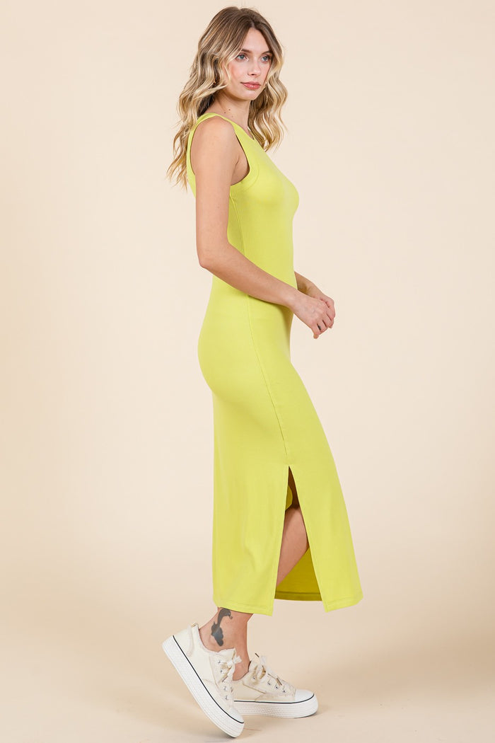 woman wearing a bright yellow sleeveless maxi dress with a side slit and paired with white sneakers