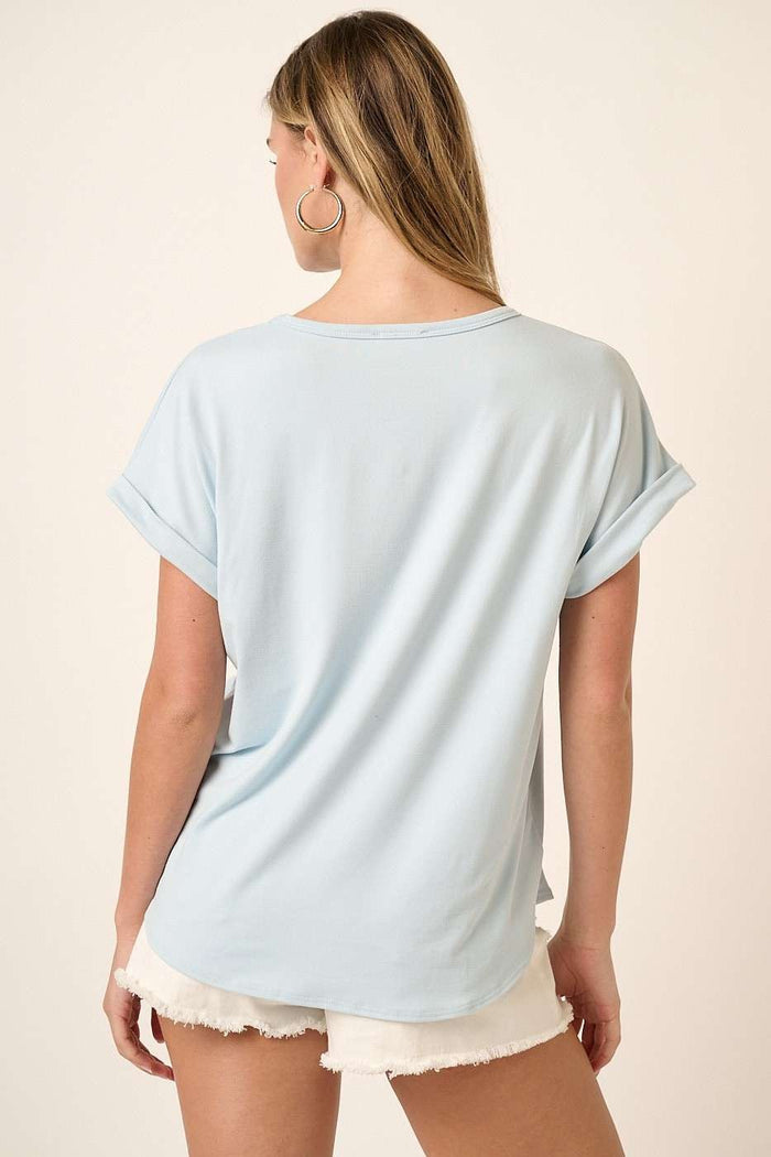 woman wearing a light blue short sleeve top with rolled cuffs and relaxed fit, standing with her back to the camera