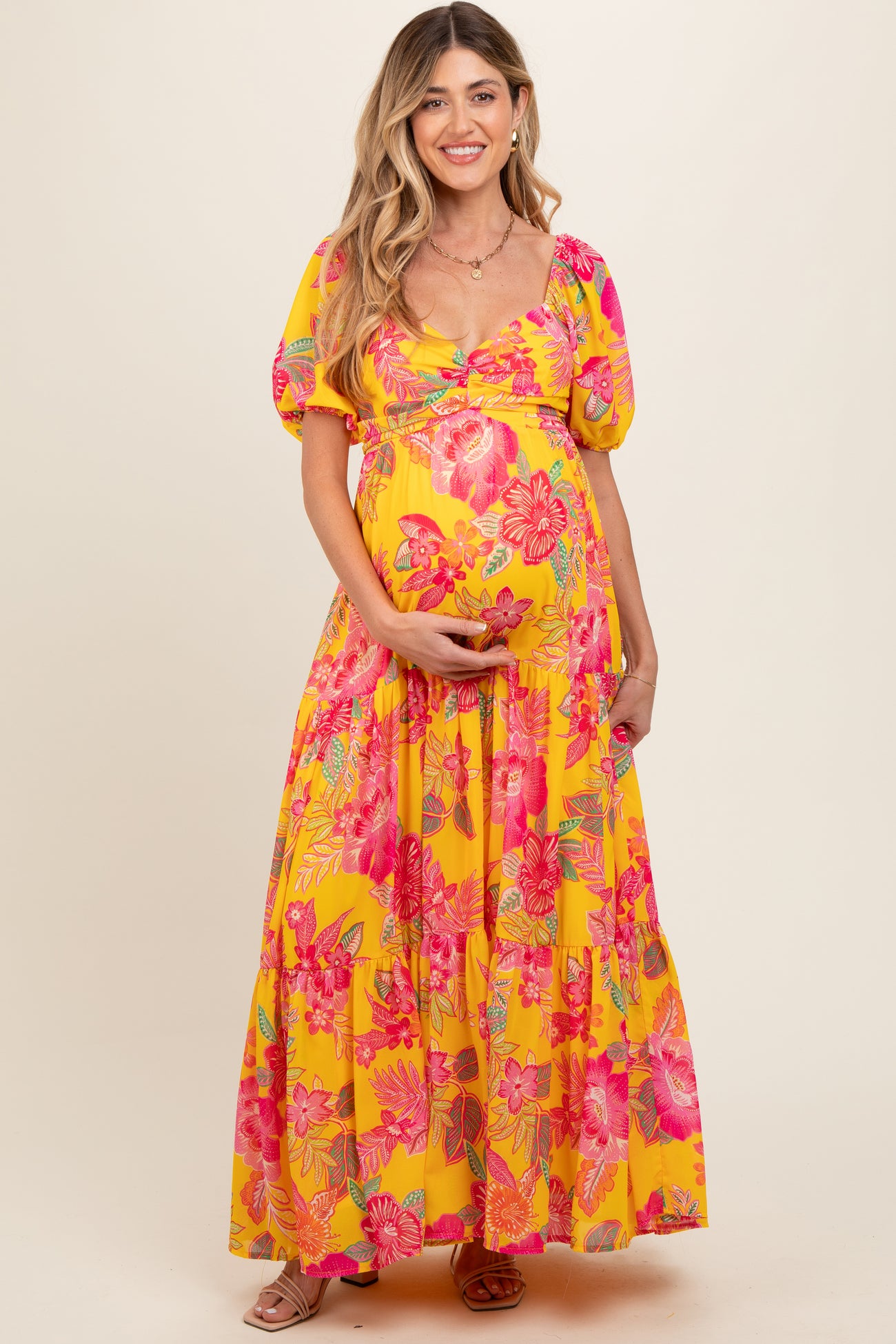 woman wearing a bright yellow floral maxi maternity dress and holding her baby bump
