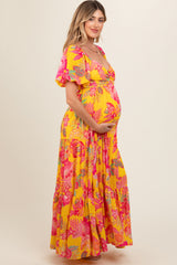 woman wearing a bright yellow floral maternity maxi dress and holding her baby bump