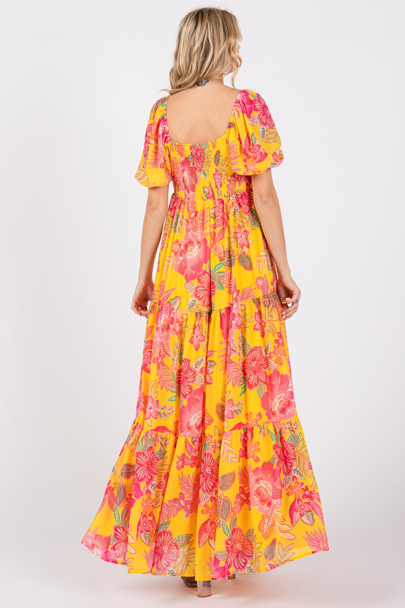 woman wearing a yellow floral maxi dress with puff sleeves and tiered skirt, viewed from the back