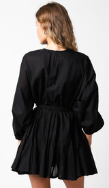 woman wearing a black belted mini dress with long sleeves and a pleated skirt, view from the back