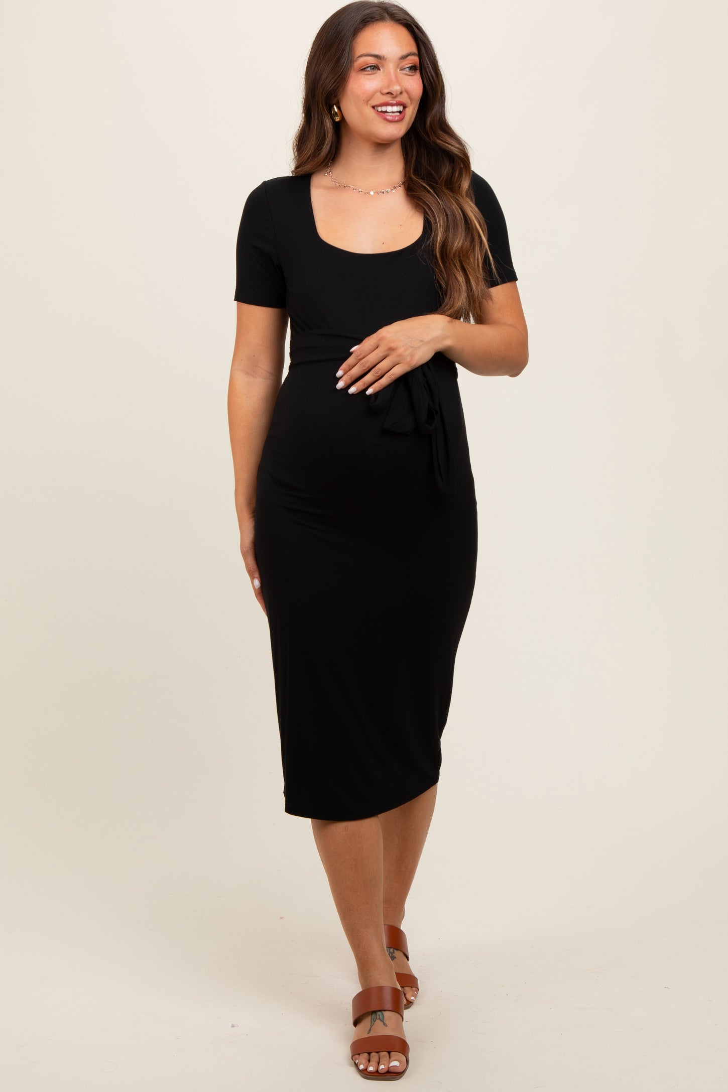 woman wearing a black short sleeve maternity dress with a scoop neckline and tie detail at the waist, showcasing her baby bump