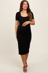 woman wearing a black short sleeve maternity dress with a scoop neckline and tie detail at the waist, showcasing her baby bump