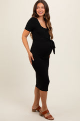 woman wearing a black maternity dress with a tie detail at the waist and a visible baby bump