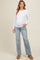woman wearing a white long sleeve maternity top and distressed light blue jeans with a visible baby bump