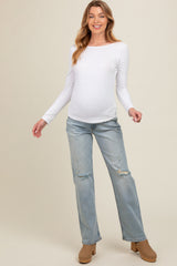 woman wearing a white long sleeve maternity top and distressed light blue jeans with a visible baby bump
