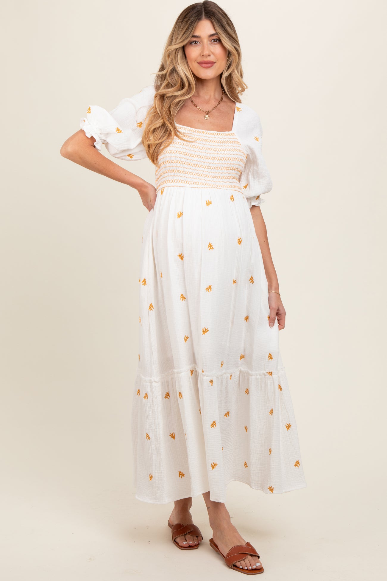 woman wearing a white maternity dress with floral embroidery and puff sleeves, showcasing her baby bump