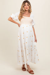 woman wearing a white maternity dress with floral embroidery and puff sleeves, showcasing her baby bump