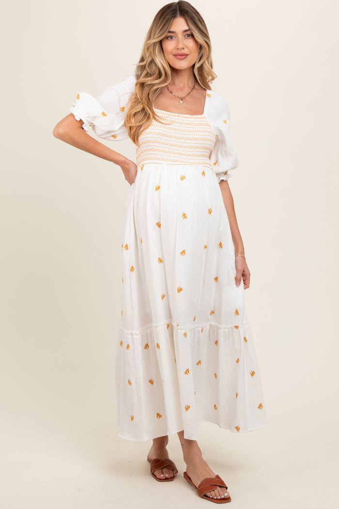 woman wearing a white maternity dress with floral embroidery and puff sleeves, showcasing her baby bump