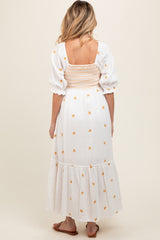 woman wearing a white maternity dress with orange floral embroidery and puff sleeves, showcasing a smocked back design