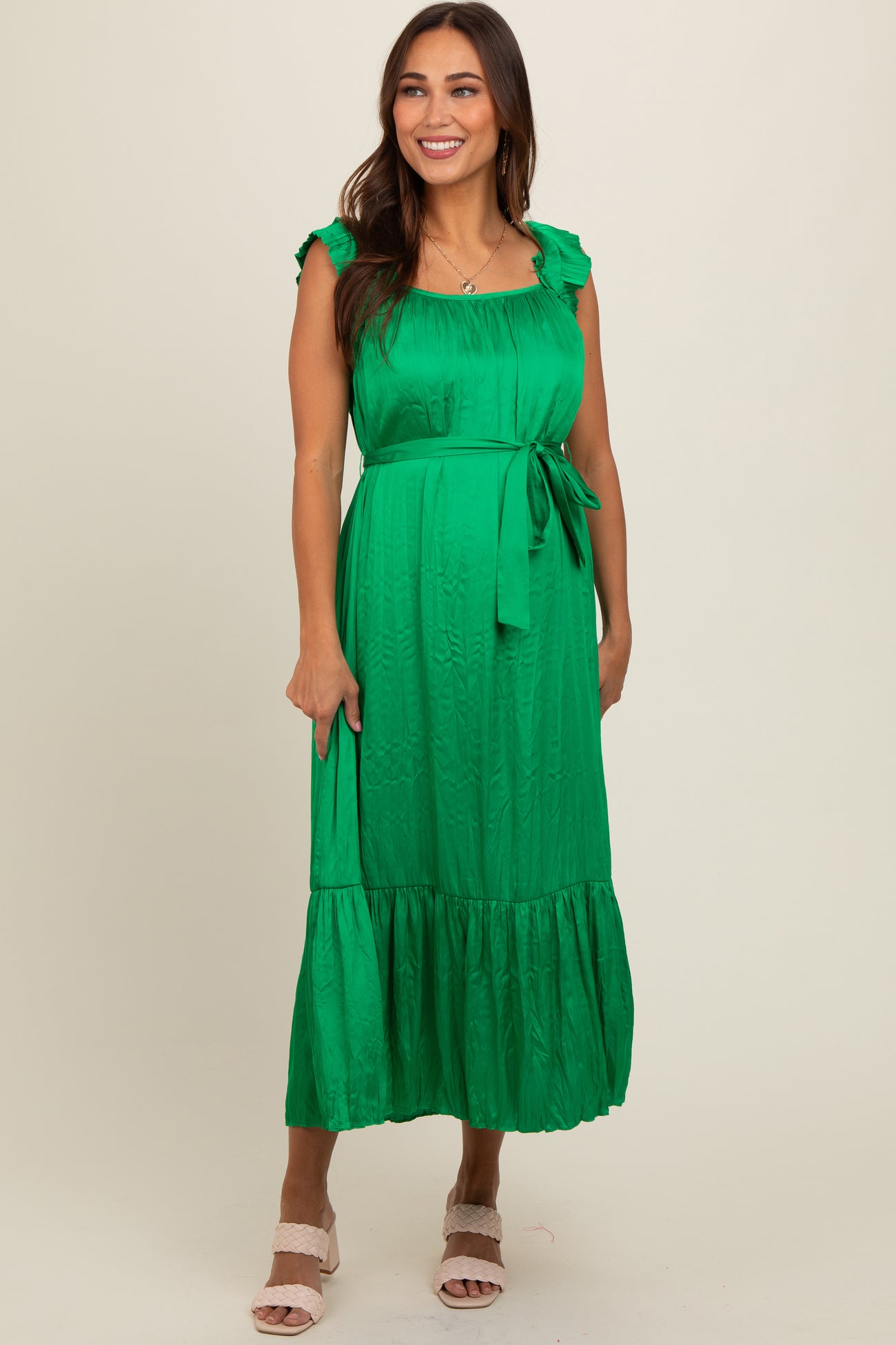 woman wearing a green maternity dress with ruffle details and a tie waist, standing and smiling