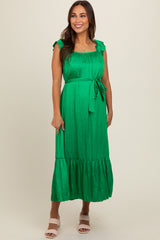 woman wearing a green maternity dress with ruffle details and a tie waist, standing and smiling