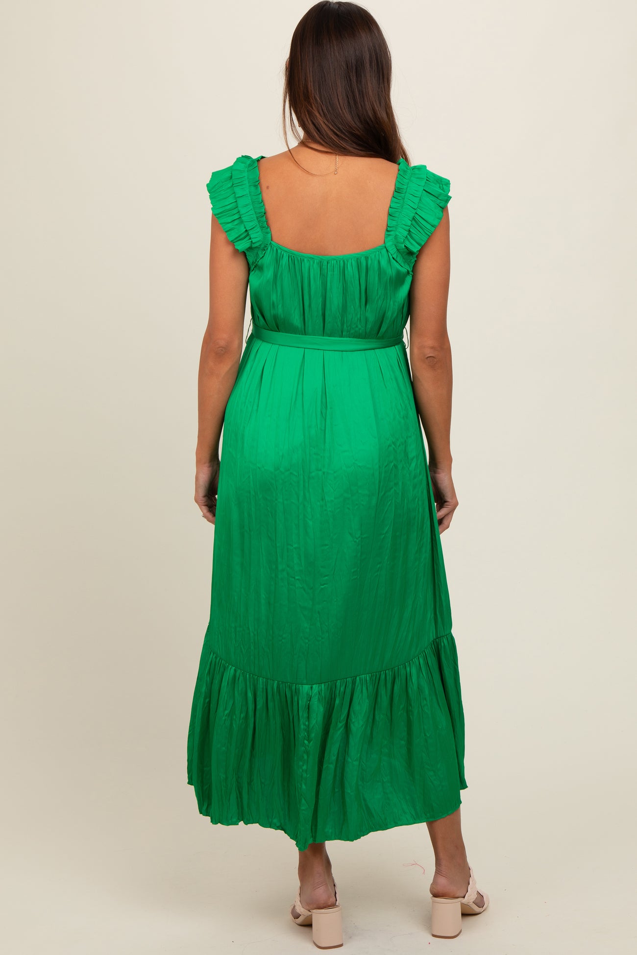 woman wearing a green maternity maxi dress with ruffle straps and a tiered skirt, showcasing her baby bump