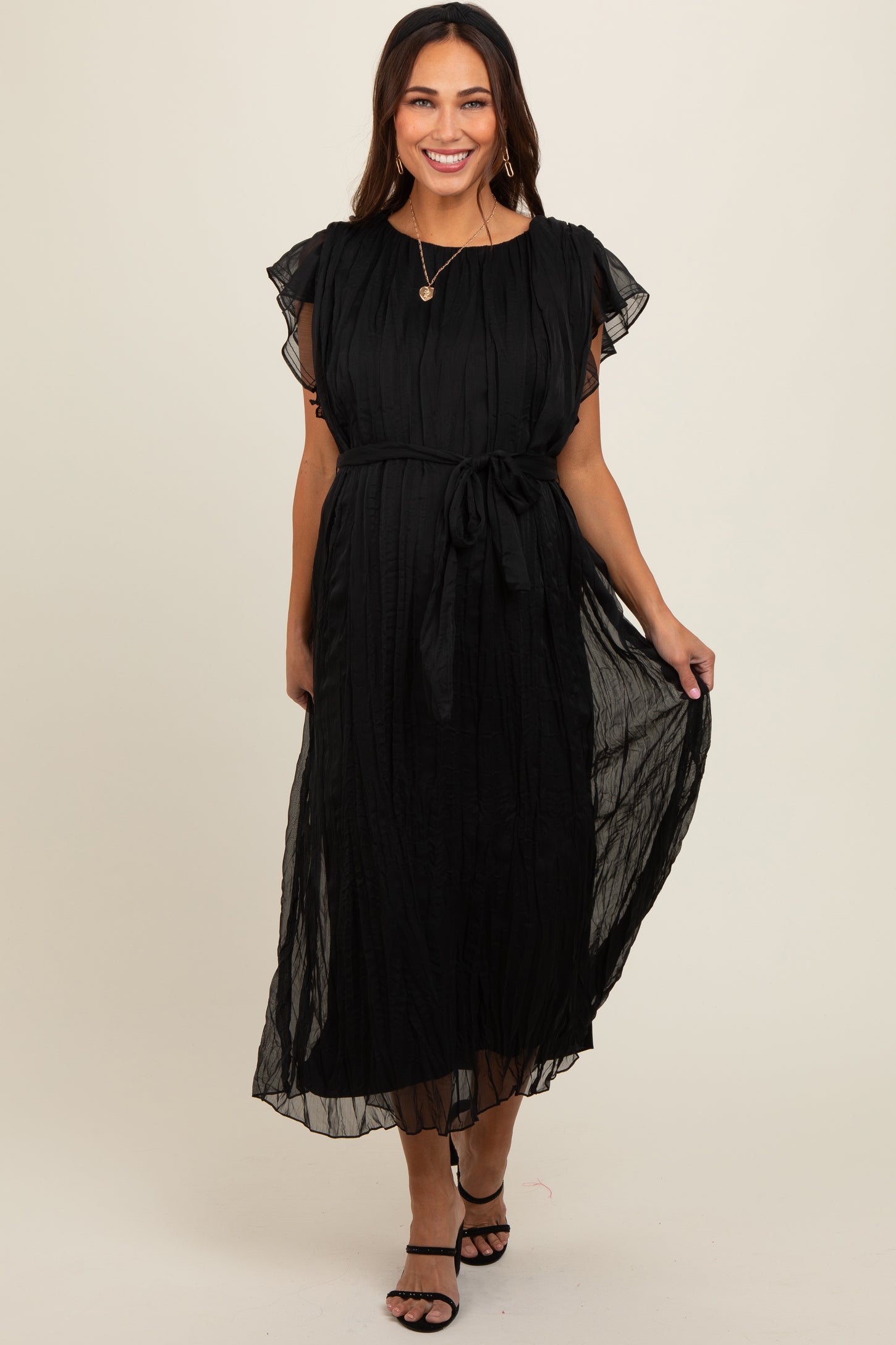 woman wearing a black maternity dress with short flutter sleeves and a tied waist detail, posing with a smile