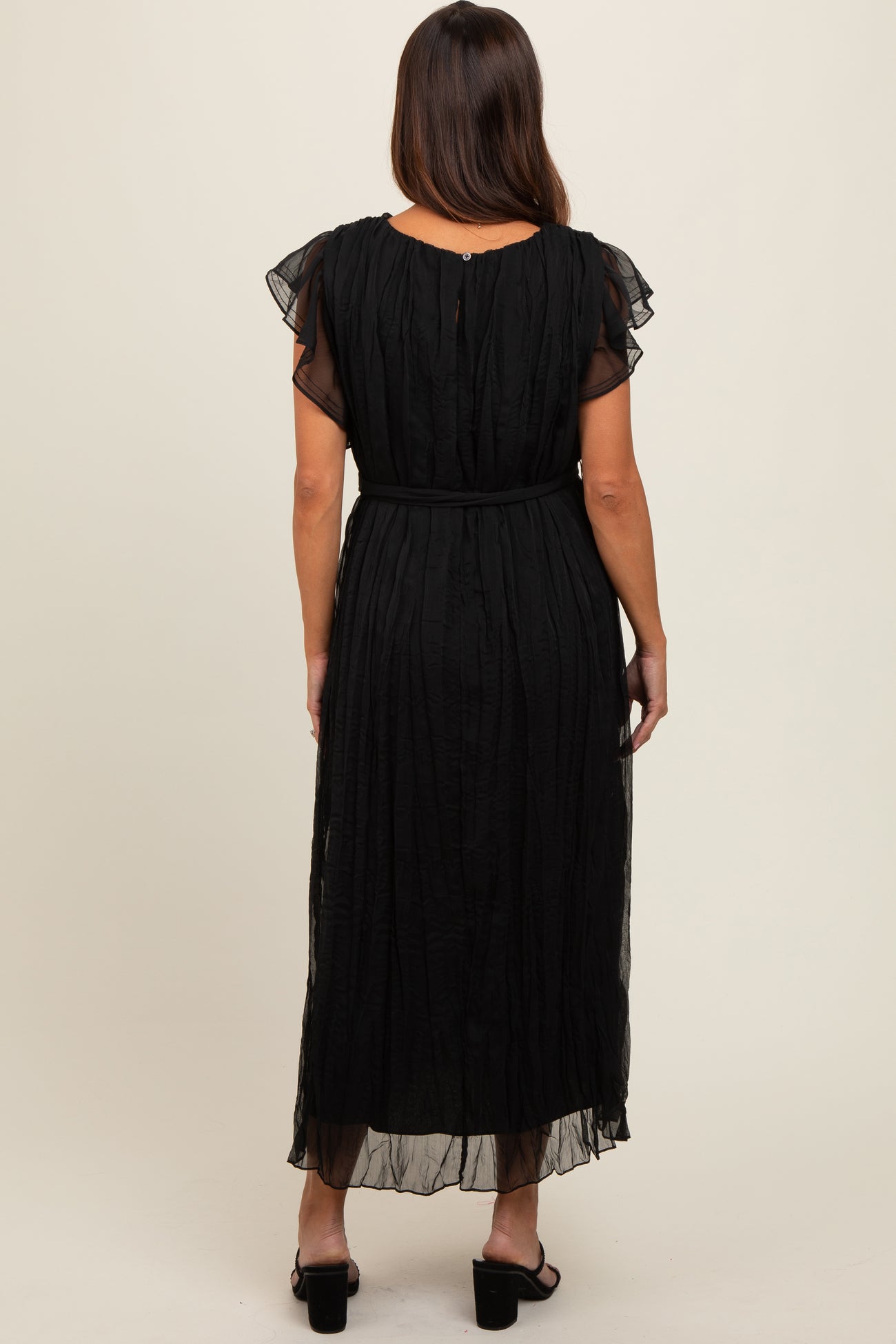 woman wearing a black maternity maxi dress with flutter sleeves and a belted waist, showing flowing fabric from the back