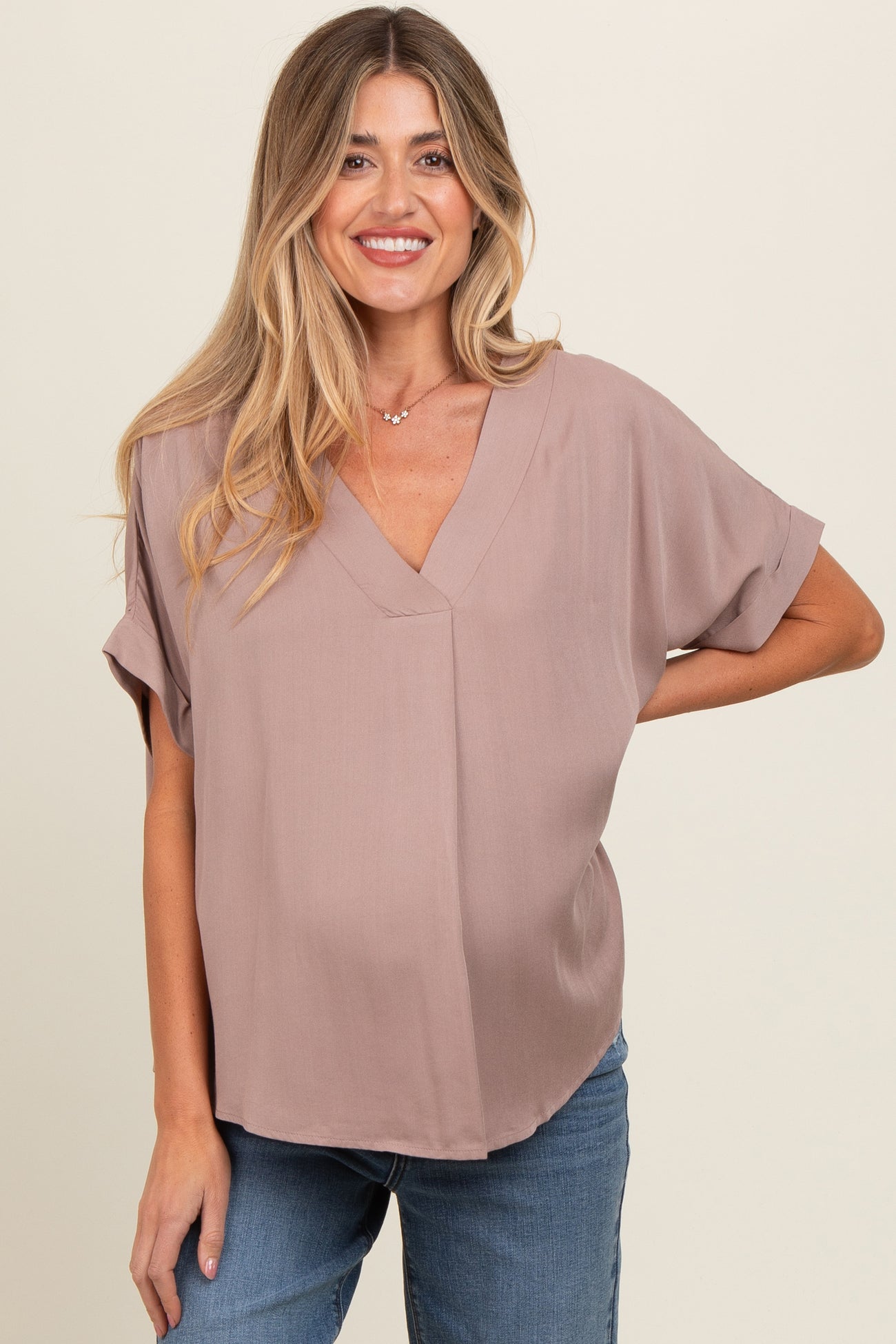 woman wearing a mauve short sleeve maternity top and smiling, showing her baby bump