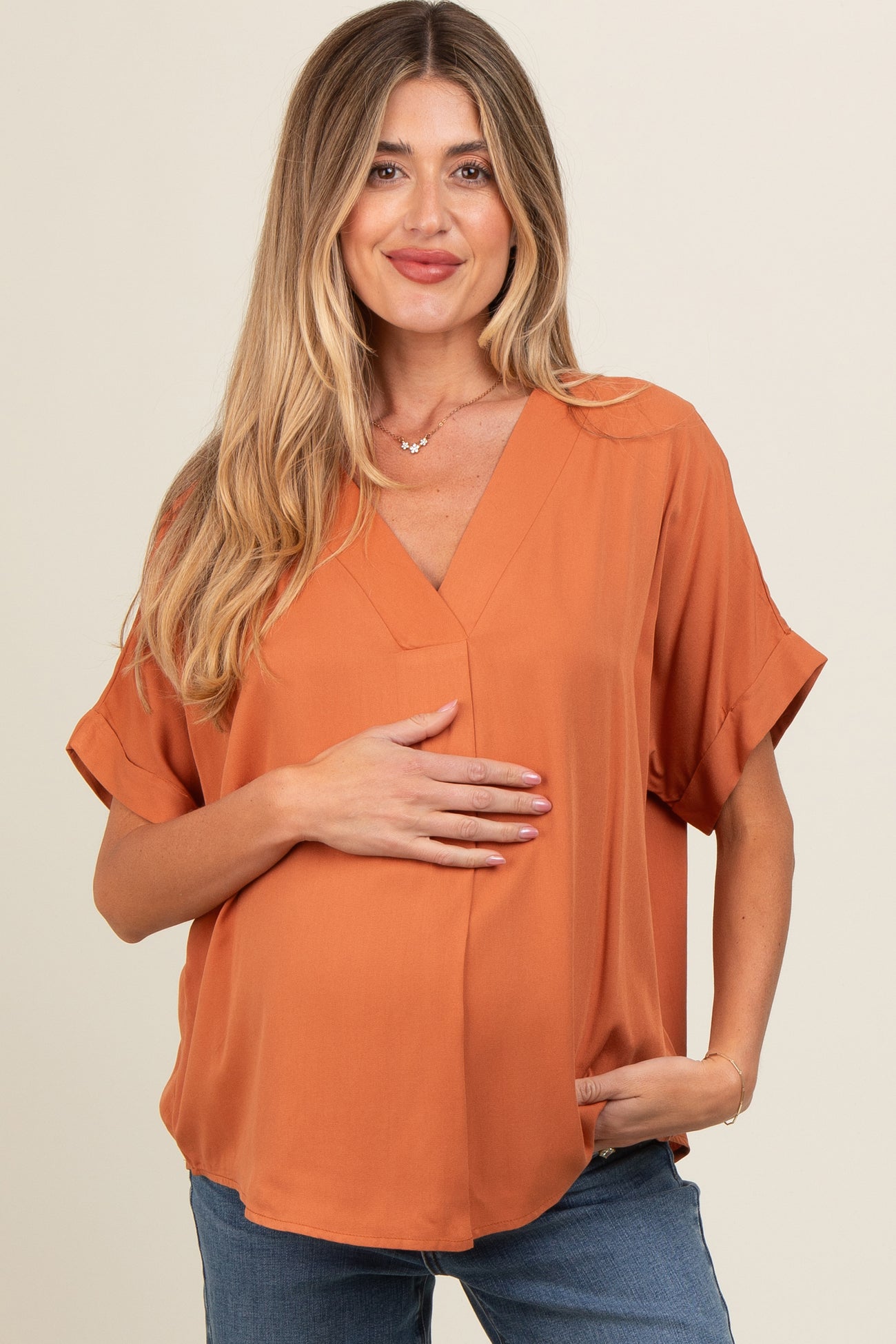woman wearing an orange maternity top with a v-neck and short sleeves, holding her baby bump