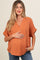 woman wearing an orange maternity top with a v-neck and short sleeves, holding her baby bump