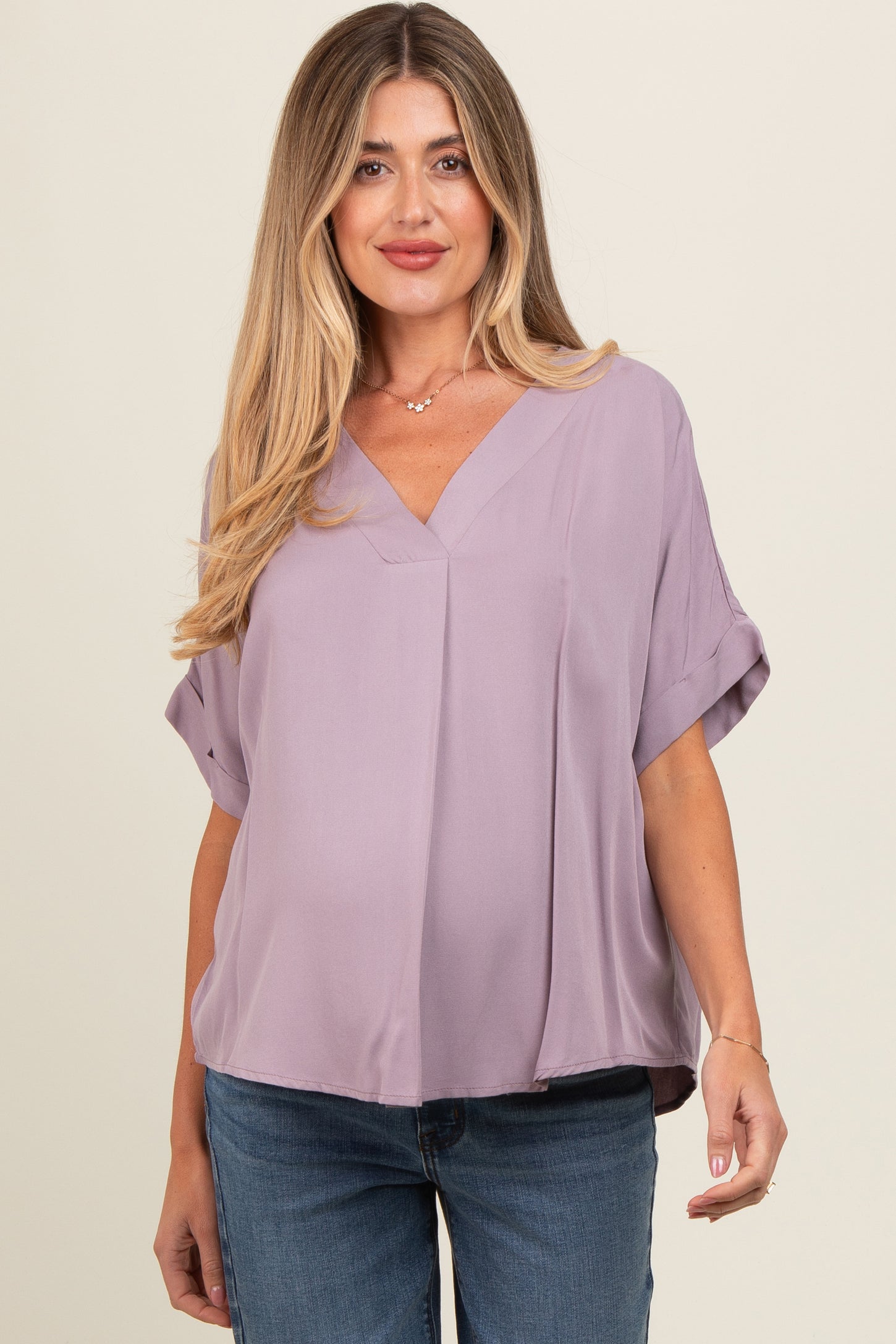 woman wearing a lavender short sleeve maternity top with a v-neck and loose fit, smiling at the camera