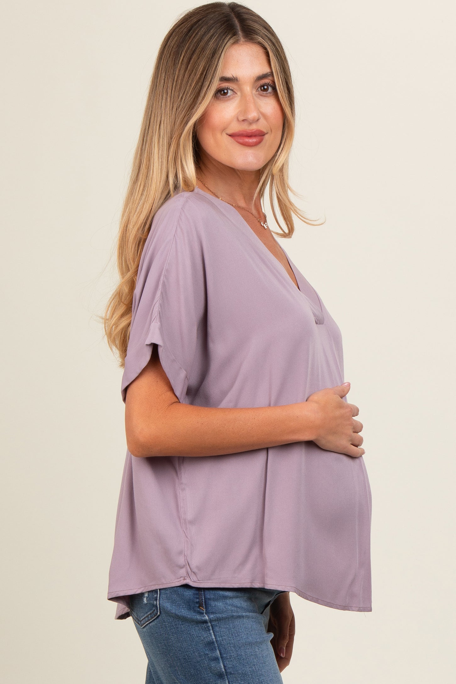 woman wearing a lavender maternity top with short sleeves and a v-neck, holding her baby bump
