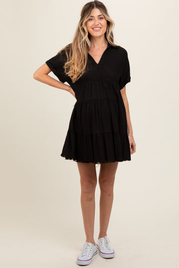 woman wearing a black tiered maternity dress with short sleeves and a v-neckline, standing in casual white sneakers
