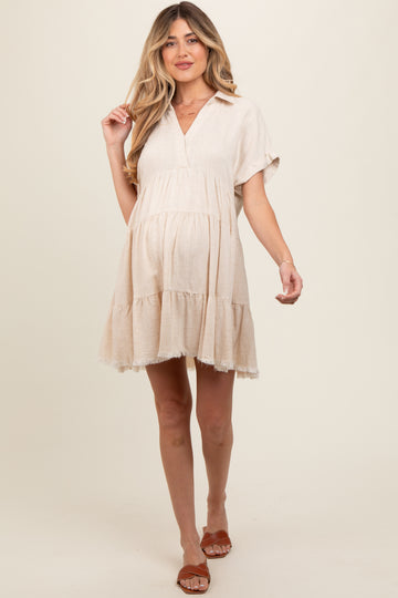 woman wearing a beige maternity dress with a tiered hem and short sleeves, showing her baby bump