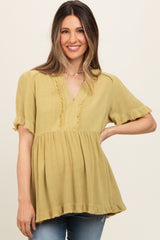 woman wearing a mustard yellow maternity top with a v-neck and ruffled hem, smiling at the camera