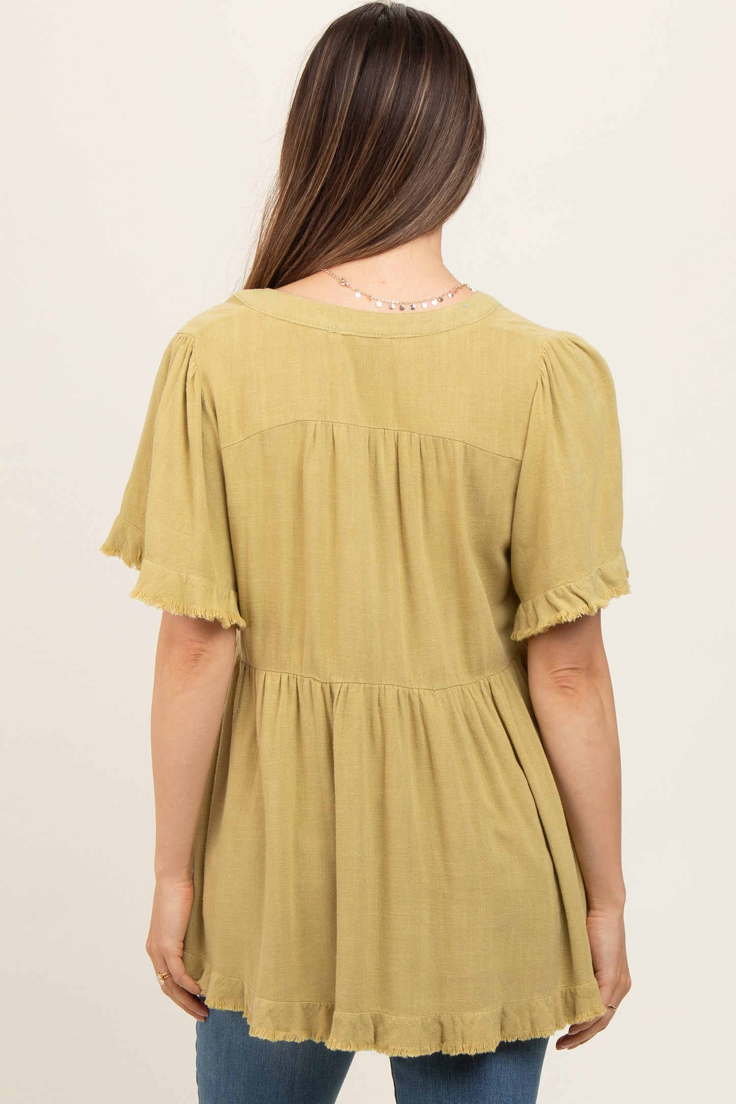 woman wearing a mustard yellow maternity top with short ruffled sleeves and a tiered hem, viewed from the back
