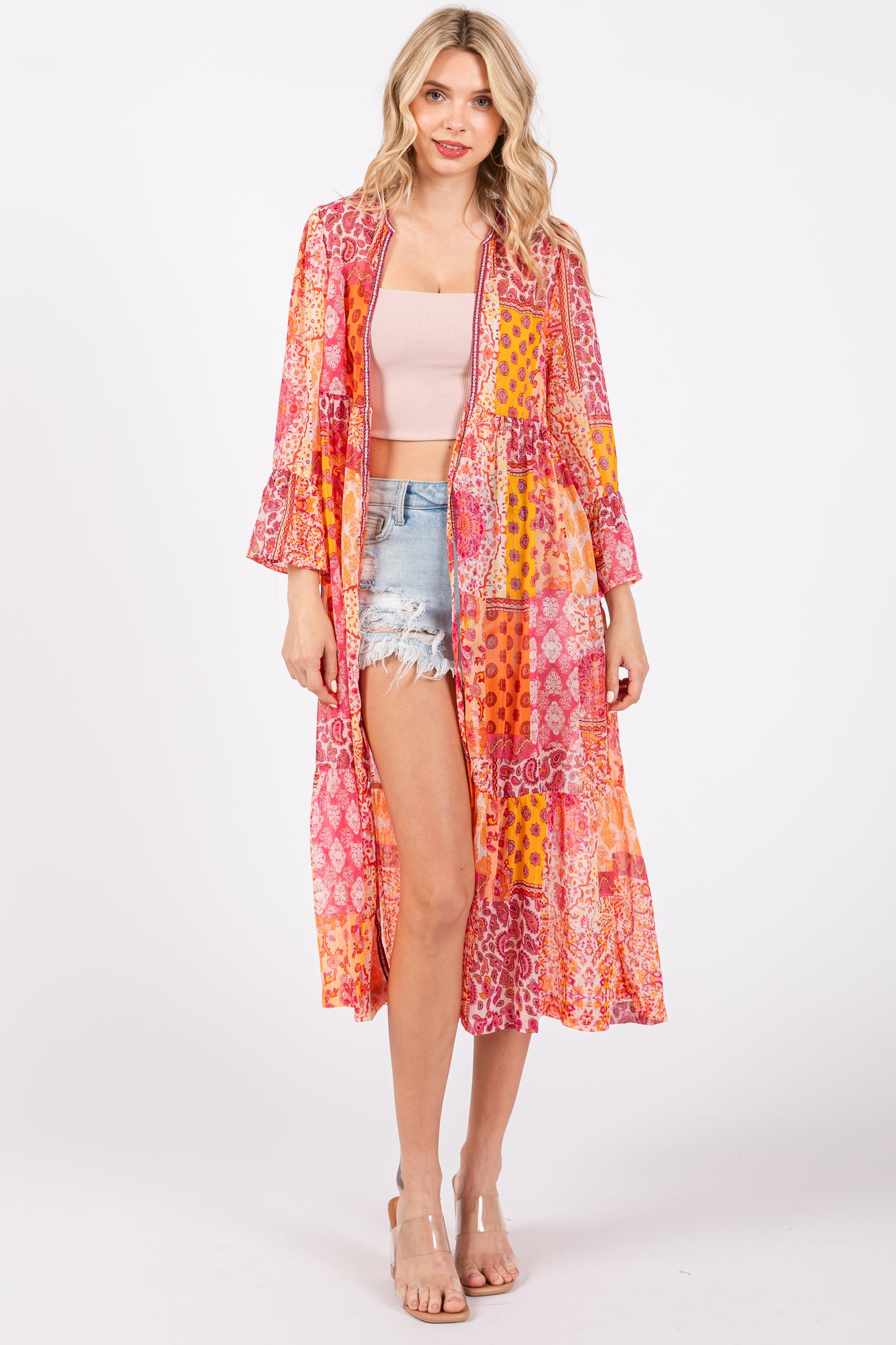 woman wearing a colorful long kimono jacket over a pink crop top and denim shorts
