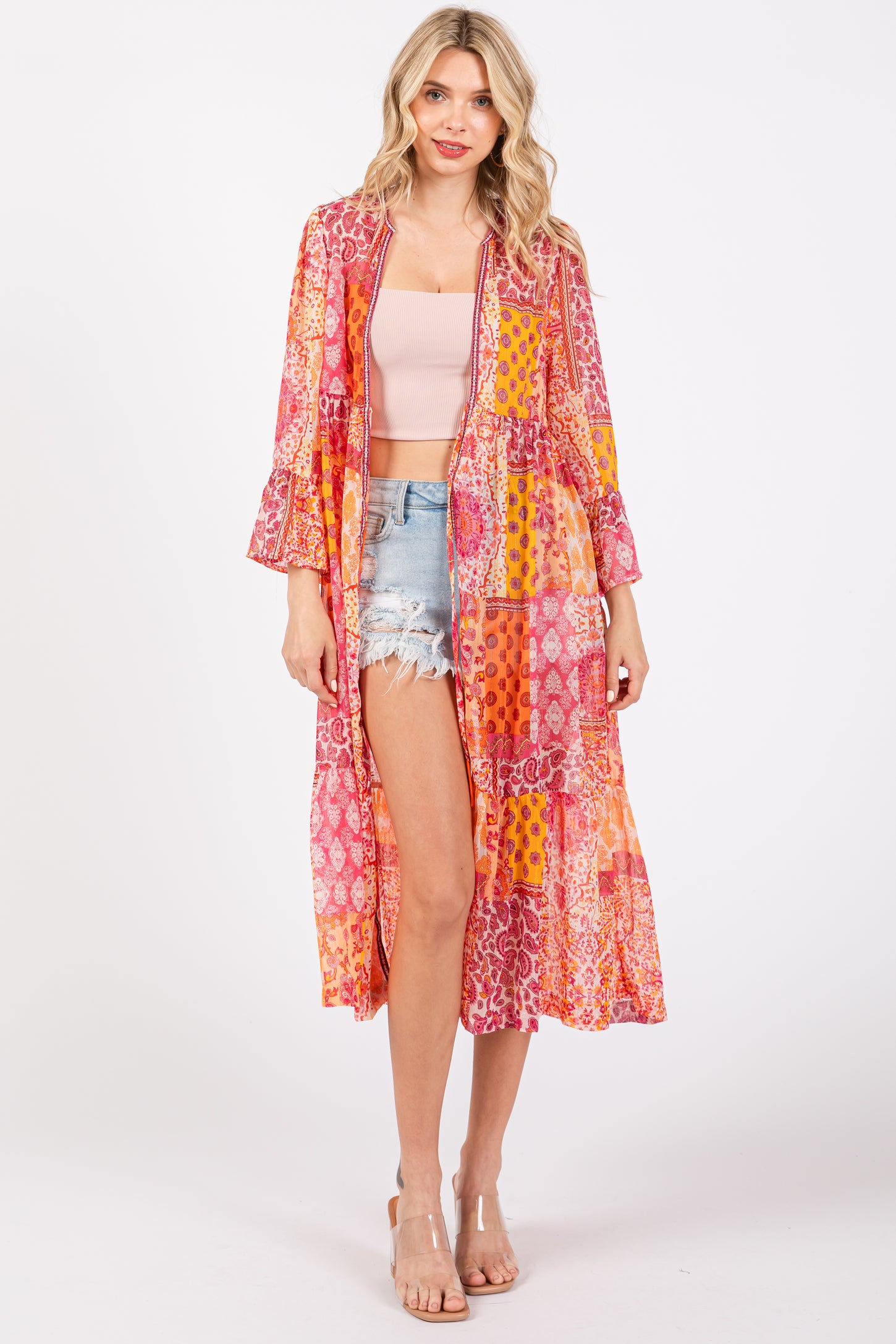woman wearing a colorful long kimono jacket over a pink crop top and denim shorts