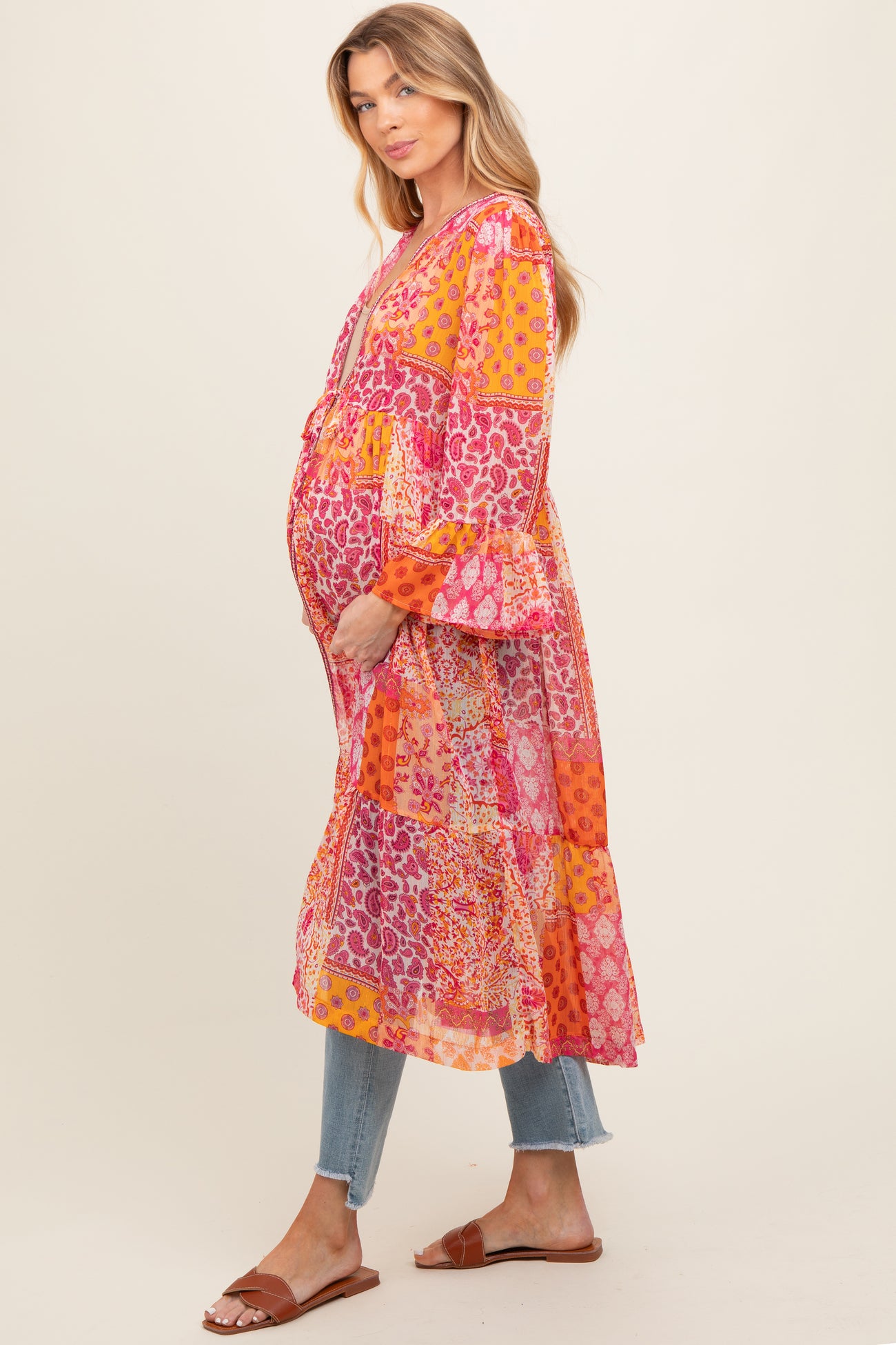 woman wearing a colorful patchwork maternity dress with long sleeves and a flowing design, showing her baby bump