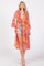 woman wearing a colorful patterned long kimono with bell sleeves over a pink tank top and denim shorts