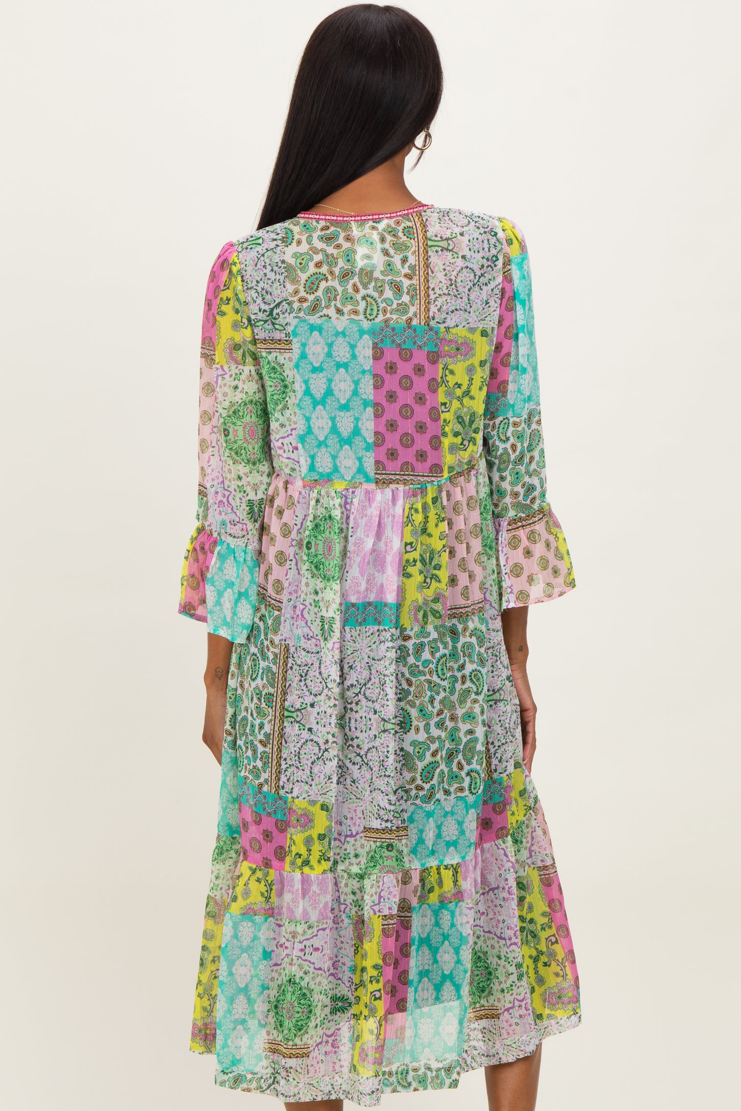 woman wearing a colorful patchwork midi dress with flared sleeves and a tiered hem, shown from the back