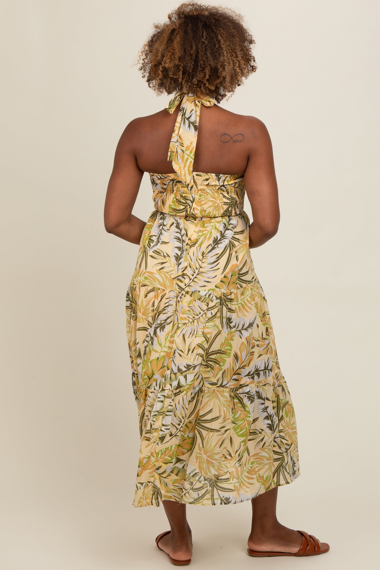 woman wearing a sleeveless yellow tropical print maxi dress with a halter neck and a flowy skirt, shown from the back