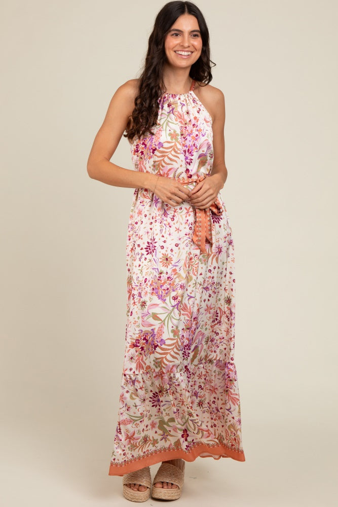 woman wearing a floral print halter neck maxi dress with an orange hem and holding it at the waist