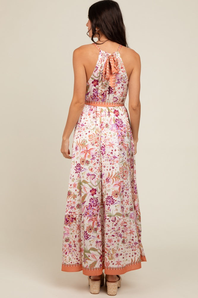 woman wearing a floral maxi dress with a back tie detail and a flowy skirt in pink and cream tones