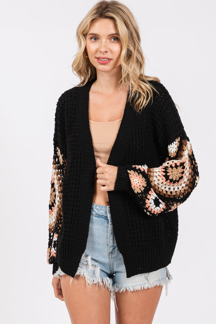 woman wearing a black chunky cardigan with crochet pattern sleeves and styled with a beige top and denim shorts