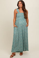 woman wearing a green floral maternity maxi dress with a square neckline and pockets, showcasing a baby bump
