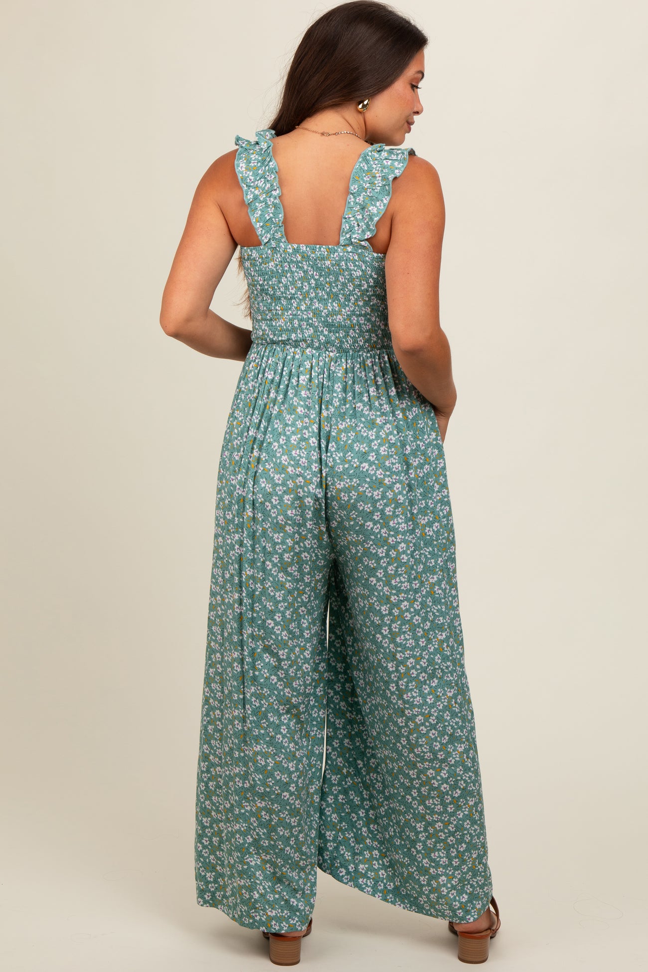 woman wearing a green floral maternity jumpsuit with ruffled straps and a smocked back, showing a baby bump